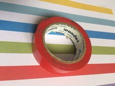 a roll of red tape sitting on top of a colorful striped tablecloth covered floor