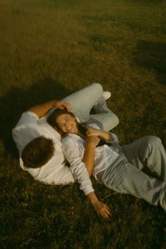 two people laying in the grass with their arms around each other and one person holding his head