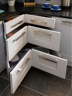 an open drawer in the corner of a white kitchen cabinet with black counter tops and drawers