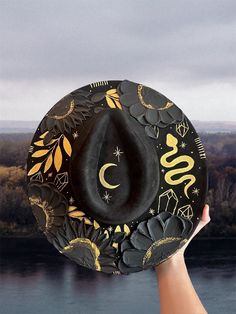 Halloween hat Brim is about 3.75" wide  Content: Vegan Suede Adjustable to fit your head better if needed  Elevate your style with this stunning hand-painted wide-brim fedora, crafted from luxurious vegan suede in a timeless black and gold palette. This one-of-a-kind piece is adorned with intricate designs featuring a serpent winding gracefully around the crown, sparkling crystals, celestial stars, delicate leaves, and a crescent moon. Each flower is meticulously painted with thick, textured strokes, adding a unique tactile dimension to the hat's sophisticated design. This fedora isn't just a hat; it's a wearable work of art. Perfect for making a statement at festivals, special events, or just adding a touch of magic to your everyday outfits. Whether you're dressing up or down, this versat Adjustable Fedora Felt Hat For Halloween, Adjustable Flat Brim Halloween Costume Hat, Adjustable Flat Brim Halloween Hat, Wide Brim Halloween Costume Hats And Headpieces, Adjustable Flat Brim Hat For Halloween, Adjustable Flat Brim Costume Hat, Adjustable Curved Brim Top Hat For Halloween, Halloween Adjustable Top Hat With Curved Brim, Handmade Black High Crown Top Hat