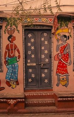 an artisticly painted building with two doors and three people on the outside, one holding a potted plant