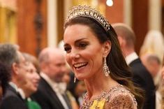 a woman in a tiara smiles as she walks down the red carpet at an event