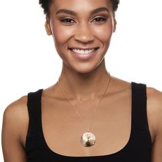 a woman wearing a black tank top smiling at the camera with a gold pendant on her neck