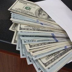 a stack of twenty dollar bills sitting on top of a desk next to a white envelope