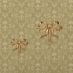 two gold bows on a green wallpaper with fleur de lis in the background