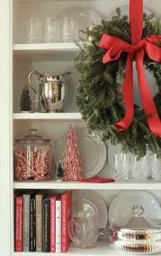 a christmas wreath on top of a white book shelf filled with books and other holiday decorations