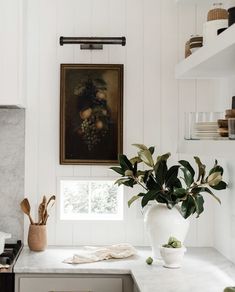 a kitchen with white cabinets and marble counter tops is pictured in this image, the painting above the stove has fruit on it