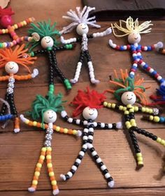 several colorful beaded dolls are arranged on a wooden table, with one person standing in the middle