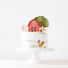 a cake decorated with farm animals and a red barn on top is sitting on a white pedestal