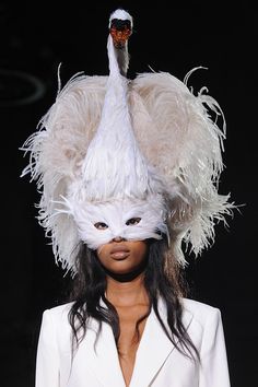 a woman wearing a white mask and feathered headdress on the catwalk