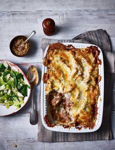 a casserole dish with meat and cheese on it next to a bowl of salad