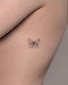 a small butterfly tattoo on the back of a woman's left side ribcage