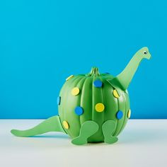 a green teapot shaped like a dinosaur with yellow and blue dots on its body