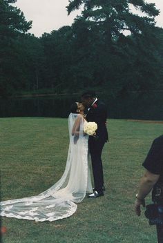 a bride and groom are kissing in the grass with trees in the backgroud