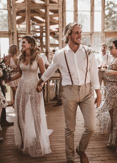 a man and woman holding hands walking down a wooden floor with other people in the background