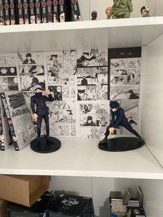 two figurines sitting on top of shelves in a room with comic books and other items