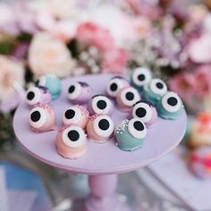 there is a purple cake with eyes on it and pink flowers in the back ground