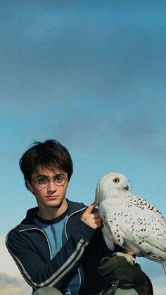 a young man holding an owl on his arm in front of a blue and white sky