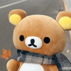 a brown teddy bear with a scarf around its neck and an orange maple leaf in the foreground