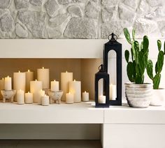 many lit candles sit on a white shelf next to a cactus and potted cacti