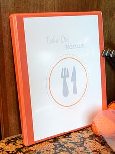 an orange and white menu sitting on top of a table next to utensils