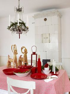 a dining room table set for christmas with red dishes and plates on it, surrounded by holiday decorations