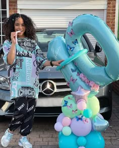 a woman standing in front of a car holding up an air filled number sixty balloon