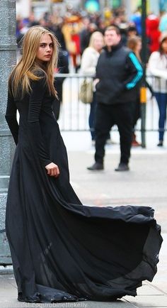 a woman in a long black dress standing next to a pole