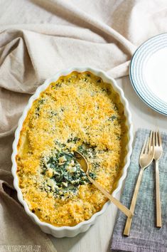 a casserole dish with spinach and cheese in it on a table next to silverware