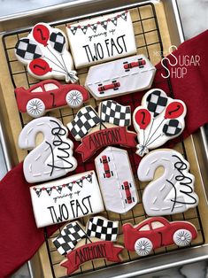 decorated cookies in the shape of race cars on a cookie sheet with red ribbon and white icing