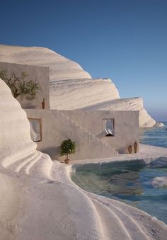 a house built into the side of a cliff by the ocean with a tree growing out of it