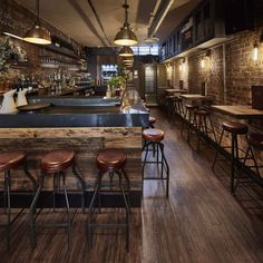 an empty bar with stools and wooden tables in the center, along with brick walls