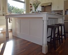 an island in the middle of a kitchen with two stools and a vase on it