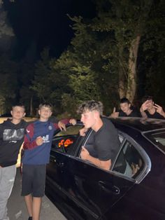 a group of young men standing next to each other in front of a black car