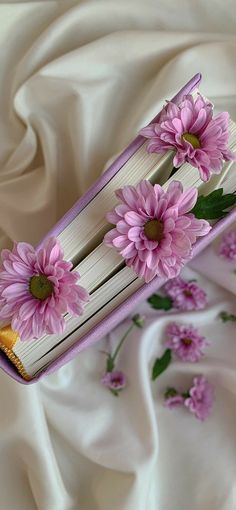 a book with pink flowers on it laying on a white cloth covered bed sheet,