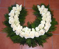 white roses and greenery arranged in the shape of a letter o on a tile floor