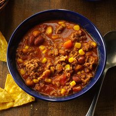 a blue bowl filled with chili and corn next to tortilla chips