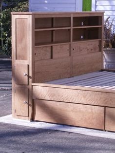 a wooden bed frame with drawers on the top and bottom side, in front of a house