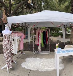 a white tent with clothes hanging from it's sides and a table on the other side