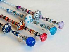 several different colored glass bead necklaces on a white surface with blue beads and silver pins