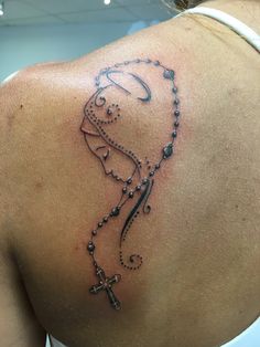 the back of a woman's shoulder with a cross and beads tattoo on it