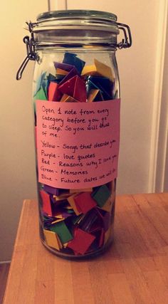 a jar filled with lots of colorful paper stuck to it's side on top of a wooden table