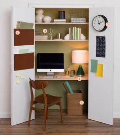 a desk with a computer on top of it in a small room next to a wall mounted clock