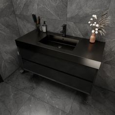 a bathroom sink sitting on top of a black counter next to a vase with flowers