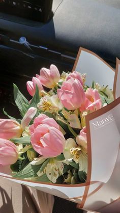 a bouquet of pink tulips and other flowers in a vase on the dashboard of a car