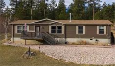 a mobile home sits on gravel in front of some trees and grass with stairs leading up to it