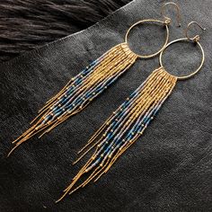 a pair of gold and blue beaded earrings on top of a black leather surface