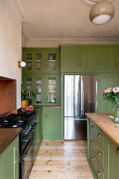 a kitchen with green cabinets and stainless steel refrigerator freezer, wood flooring and wooden counter tops