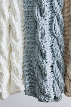 four different colors of knitted blankets hanging from hooks