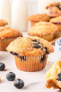 blueberry muffins on a white surface with fresh blueberries scattered around them